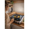 Femme en pull beige utilisant le four nomade TANDOOR sur une plaque de cuisson à gaz dans une cuisine de van aménagé