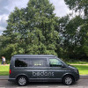 Volkswagen Transporter T5 noir avec fenêtre latérale coulissante, vue 3/4 avant sur un quai portuaire
