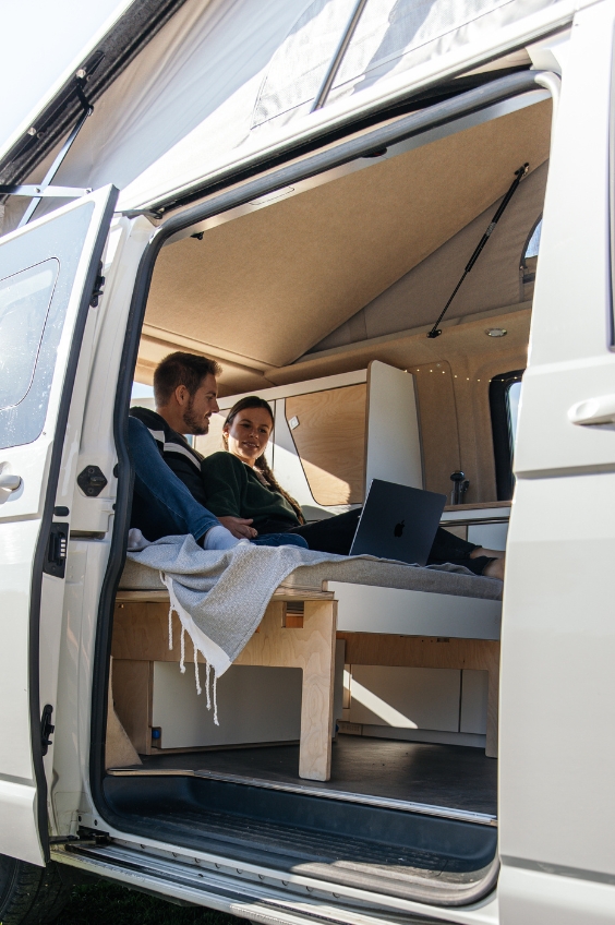 Paar nutzt den ausgebauten Van mit dem Longbed, von der Seitentür aus gesehen